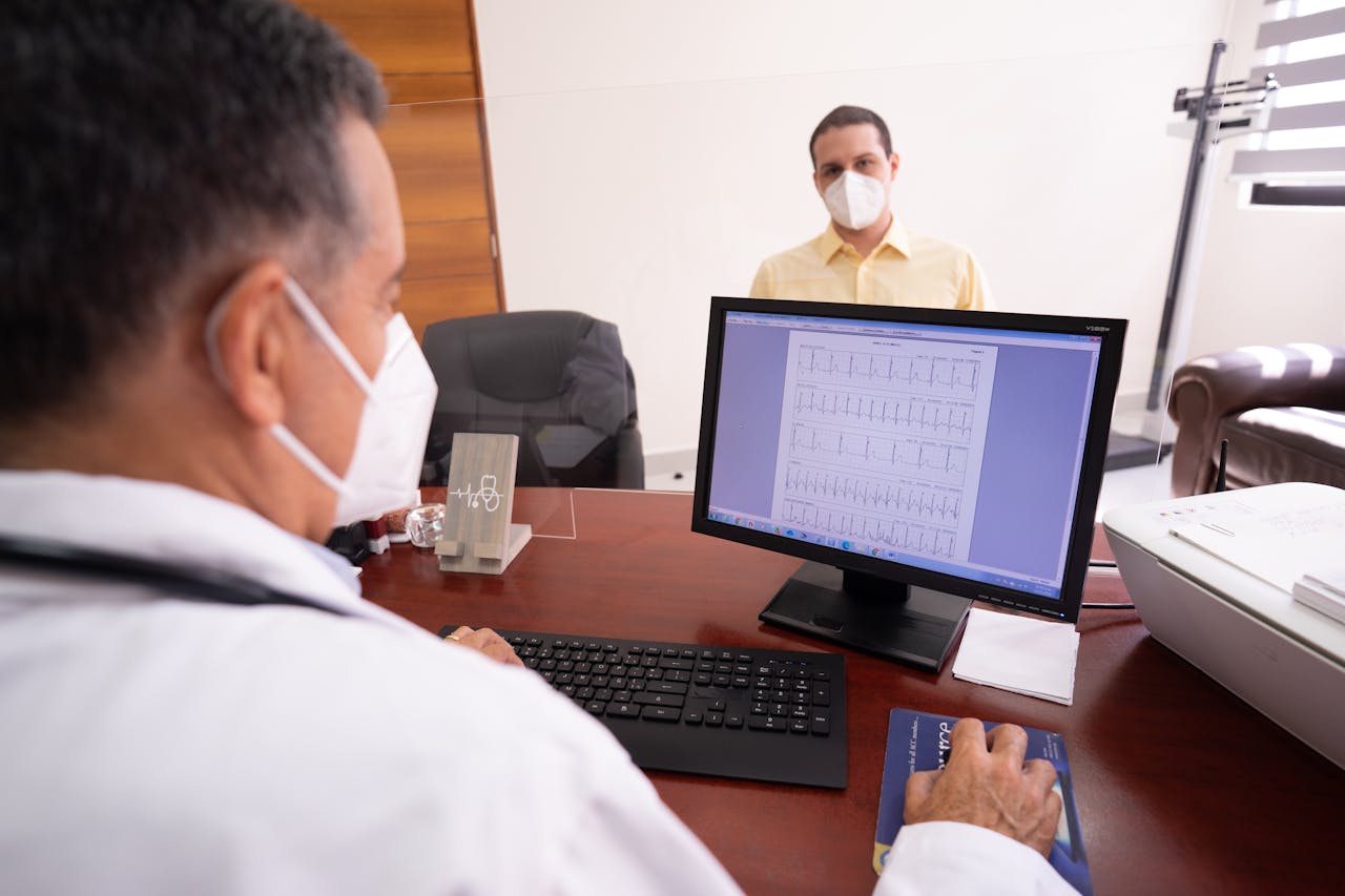 Doctor consults patient remotely using computer and face masks for safety.